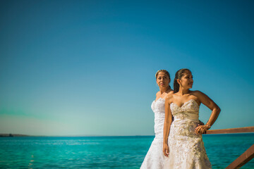 mujeres jovenes usando sus vestidos de boda a la orilla de la playa y mirando a los costados