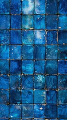 A weathered mosaic of cracked and distressed ceramic tiles in various shades of blue, creating an aged and visually striking textural backdrop. - obrazy, fototapety, plakaty