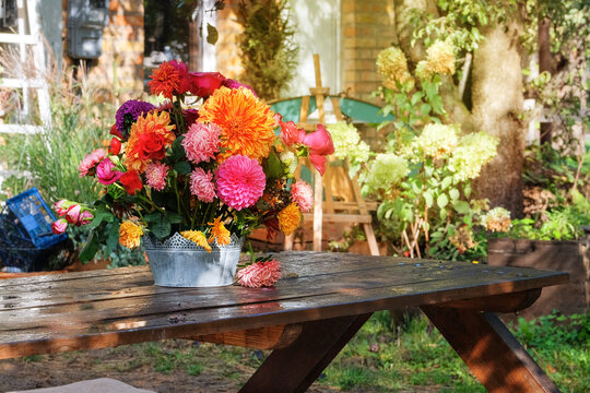 Roses, asters, dahilia in the apple garden on a wooden table. Floristic design. Flowers in sunny day. Country life. Sunny.