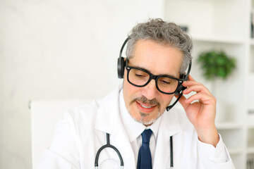A senior doctor is fully engaged in a telehealth call, wearing a headset and using a laptop, showcasing how modern technology is used in patient consultations and healthcare communication.