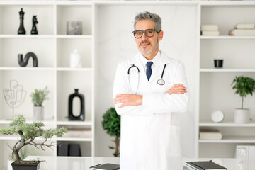 Confident mature doctor stands confidently in office, arms crossed, representing medical expertise. His smile and casual stance make for a friendly and reassuring presence in the clinical environment