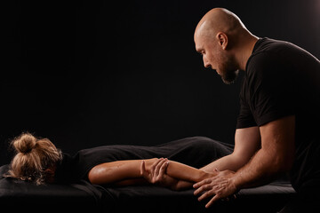 male masseur giving a hand massage to a girl on a dark background, hand massage - obrazy, fototapety, plakaty