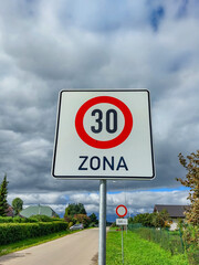 Metal road or traffic sign with number 30 in a red circle, and zone, indicating speed limit against blue sky and clouds background