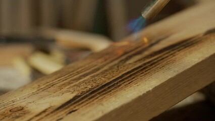 Male woodworker working in garage. Man professional carpenter working with wooden materials in workshop burning piece of wood with gas torch, close up.
