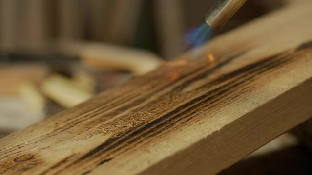 Male woodworker working in garage. Man professional carpenter working with wooden materials in workshop burning piece of wood with gas torch, close up.