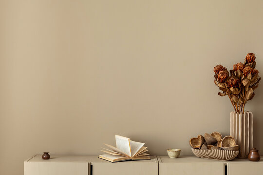 Minimalist composition of living room interior with copy space, simple beige sideboard, vase with dried flowers, books and personal accessories. Home decor. Template.