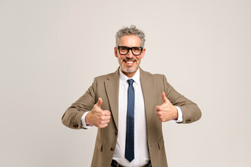 A mature businessman in a beige suit and a blue tie gives a double thumbs up, signaling success and approval, perfect for themes of achievement, positive feedback, or endorsing products and services
