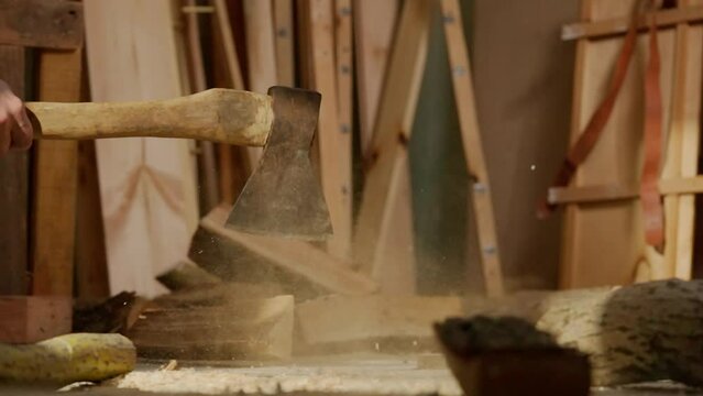 Male woodworker working in garage. Man professional carpenter working with wooden materials in workshop chopping wood using axe.