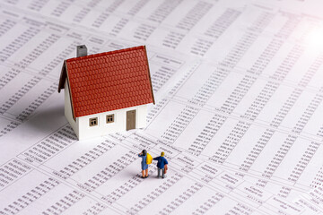 Figurines d'homme et de femme devant une petite maison individuelle sur un document d'échéancier de prêt immobilier. Concept d'achat immobilier à crédit, de durée et de taux d'intérêt d'emprunt