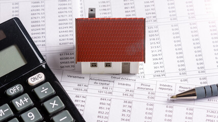 Calculette, stylo et maquette de maison individuelle posés sur un document bancaire d'échéancier de prêt immobilier. Concept d'achat immobilier à crédit, de durée et de taux d'intérêt d'emprunt