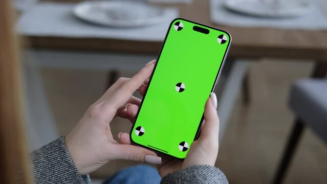 Woman using smartphone vertical green screen. Female holding in hand portable gadget. Tracking markers. Indoors. Browsing social network, news. Mock-up for tracking. Scroll up 4K