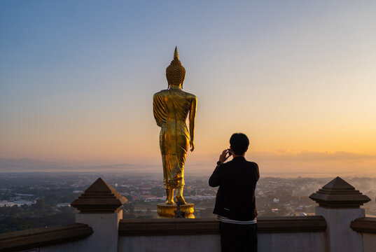 Tourists taking photos of the big Buddha statue at Wat Phra That Khao Noi, Beautiful golden morning light at viewpoint area, Nan province, Thailand.