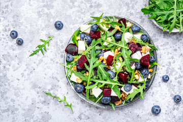 Healthy useful salad with beetroot, blueberries, feta cheese, arugula and walnuts, gray table...
