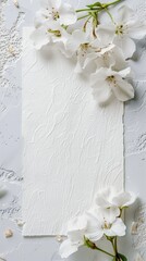 Pristine white apple blossoms with vibrant green leaves artfully arranged around a torn white paper on a textured surface.