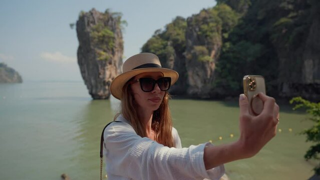 Woman travels on island Khao Phing Kan. Young female tourist sits on a boat and films take a photo selfie on beautiful mountain landscape view with rock in sea on smartphone. Travel, relaxing concept.