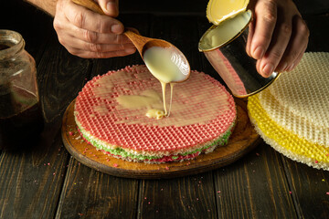 Chef hand holds a spoon with condensed milk while preparing a cake. Concept of preparing pastry...