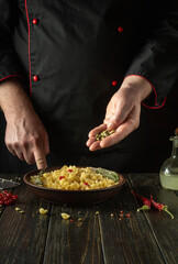 Adding aromatic spices to a bowl of pasta. The chef at the kitchen table is preparing a delicious lunch with pasta and viburnum