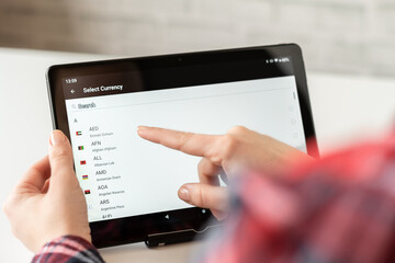 Woman finger of hand choosing foreign CHF, swiss franc currency from the list on the tablet for buying choosing online shopping, booking hotel