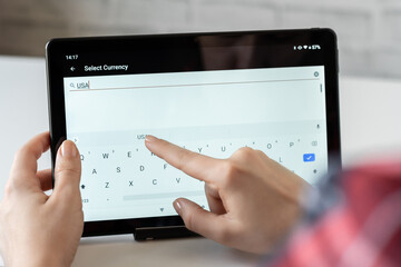 Woman finger of hand choosing foreign USA, dollar currency from the list on the tablet for buying...