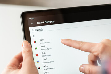 Woman finger of hand choosing foreign CHF, swiss franc currency from the list on the tablet for...