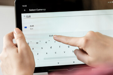 Woman finger of hand choosing foreign eur, euro currency from the list on the tablet for buying...