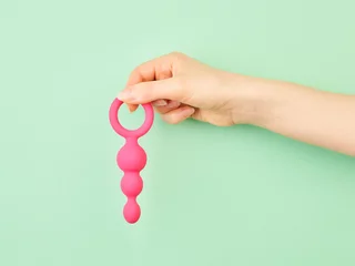 Tuinposter Woman's hand holding adult sex toy over mint background © Nik_Merkulov