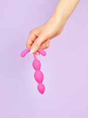 Woman's hand holding adult sex toy over violet background
