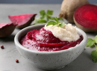 Horseradish sauce with beet in bowl and piece of beet on grey table