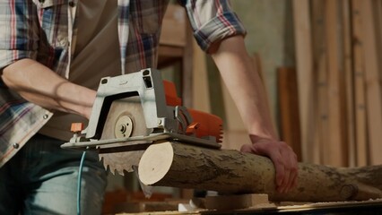 Male woodworker working in garage. Man professional carpenter working with wooden materials in workshop sawing wood using electric circular saw. - obrazy, fototapety, plakaty