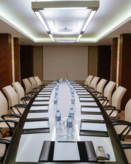 A modern conference room with a long rectangular table in the center. Numerous white leather chairs...