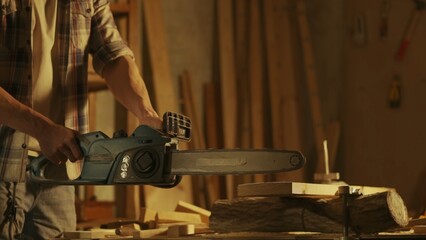 Male woodworker working in garage. Man professional carpenter working with wooden materials in workshop sawing wood using electric chainsaw.
