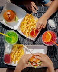 An overhead view of a table with two trays of fries, two different colored shakes, and people holding burgers.