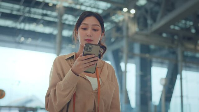 Asian tourist woman using mobile phone and watching watch between waits for flight in Airport Terminal, Browse Internet, Post on Social Media, flight check check in, Tourist journey trip concept