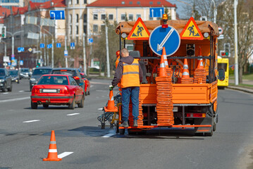 Road marking works. Workers uses  paintliner truck to apply fresh paint lines on the road. Highway maintenance, white line painting. Worker places traffic cone on fresh painted line until paint dries