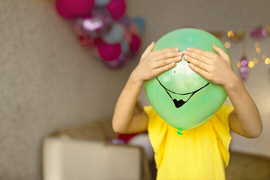 Girl in yellow dress holds balloon with drawn smiley face and closes its eyes in holiday at home. selective focus