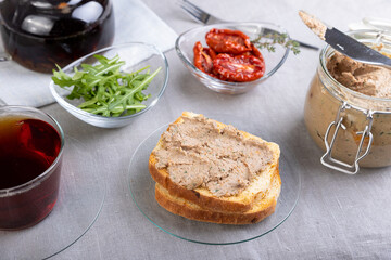 Chicken liver pate with wheat bread, arugula, sun-dried tomatoes and black tea. Homemade traditional rustic cuisine. Breakfast or snack option. Selective focus, close-up.