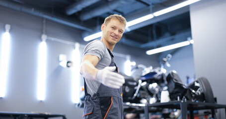 Fototapeta na wymiar Smiling young car mechanic stands in workshop. Car and motorcycle maintenance services concept