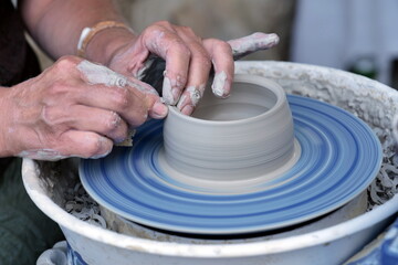 Female potter, ceramist working on pottery wheel while sitting in her workshop