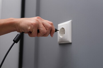 Woman hand inserts electrical plug into outlet. Correct connection of electrical appliances concept