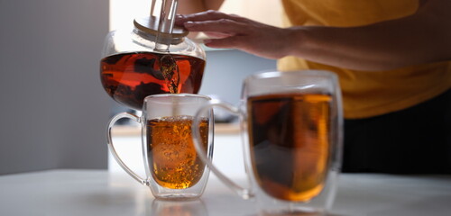 Woman pouring black tea from teapot into cup closeup. Family tea party concept