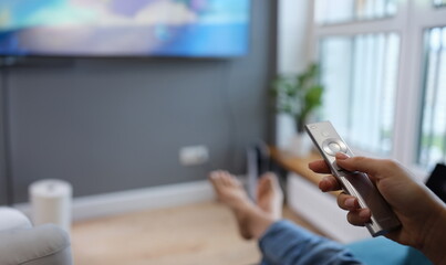 Woman is sitting on sofa and holding TV remote control in her hands closeup. Home leisure and...