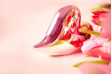 A metal heart with pink tulip flowers reflected in it. Abstract background in pink shades for the holidays of love - 779819236