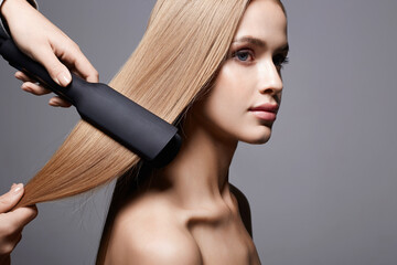 beautiful blond hair woman. Care and straightening hair with an iron