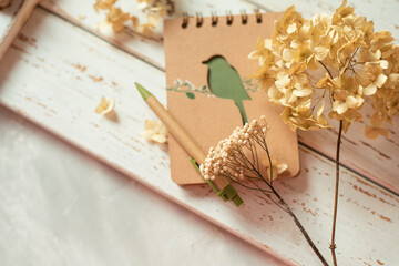 Notepad and dried flowers on a white wooden background. View from above.
