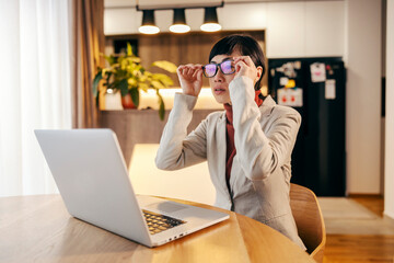 A japanese businesswoman is putting eyeglasses and reading a mail on a laptop.