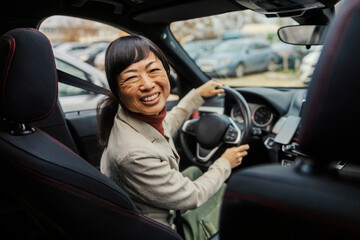 Portrait of a middle aged japanese businesswoman driving her car and smiling at the camera.