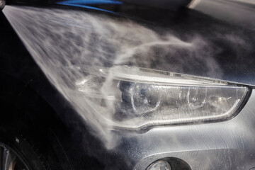 Close up of high pressure water gun cleaning car headlights.