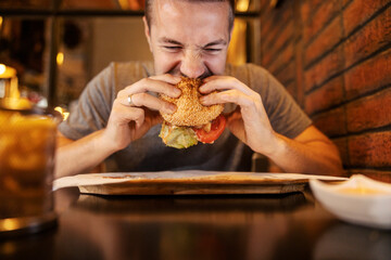 A hungry man sitting in restaurant and biting delicious hamburger.