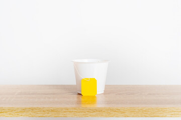 A tea bag with a blank yellow label in a cup. Cozy template with space for text on a tea bag tag.