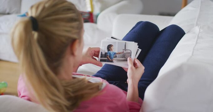 Young mother lying on sofa in living room watching printed family photos